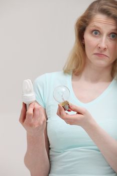 Woman holding a new efficient eco-bulb and an inefficient costly incandescent bulb with a look of complete ignorance