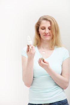 Woman holding both an eco-bulb and an incandescent bulb and frowning in disapproval at the outdated electrical technology of the latter