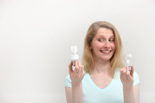 Woman holding an eco-friendly spiral bulb and an old incandescent bulb and smiling in approval of the eco bulb