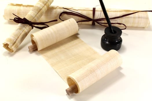 yellowed papyrus scrolls with quill and inkwell on a light background