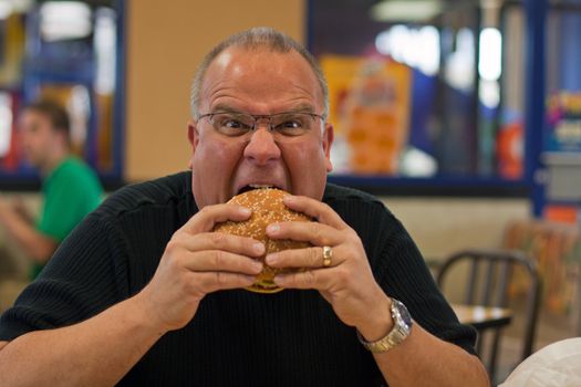 Overweight man eating burger in restaurant