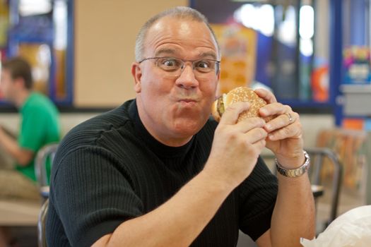 Overweight man eating burger in restaurant
