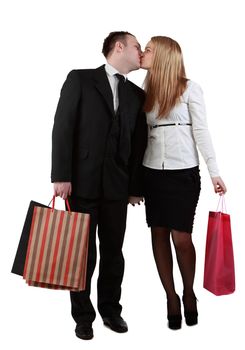 Young couple holding shopping bags and kissing against a white background.