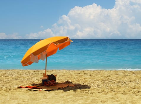 Yellow umbrella on hot sandy beach by turquoise blue ocean