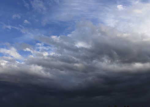 Dark rain clouds gathering on blue sky background