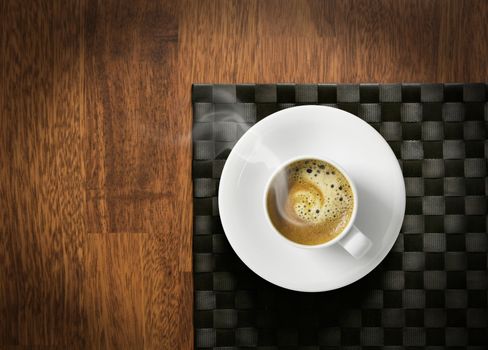 Steaming hot cup of espresso coffee with crema on wooden table and dark tablemat