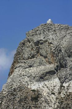 White Greek church high on steep mountain cliff peak