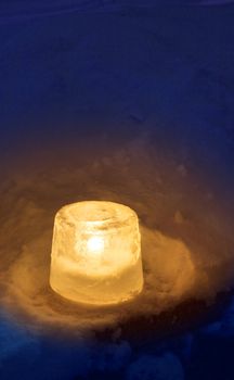 Ice lantern with candle burning in winter evening twilight