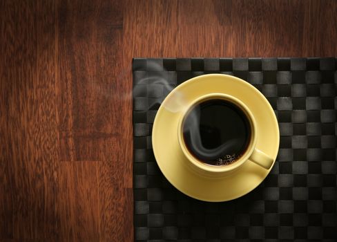 Steaming hot cup of black coffee on wooden table and dark tablemat