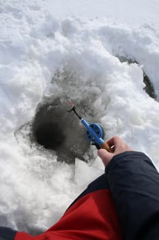 Hand holding ice fishing rod and and angling from a hole in the ice