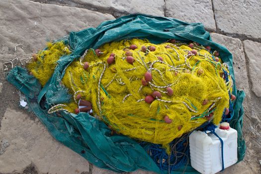 Yellow fishing nets pine, ropes and canister on stone paved ground