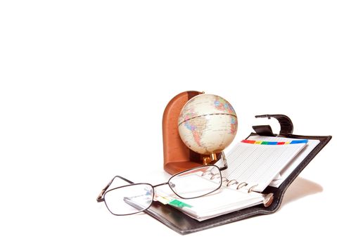 articles of office are a globe, notebook and glasses on a white background