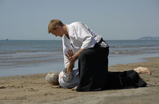 Two adults are training in Aikido on the beach