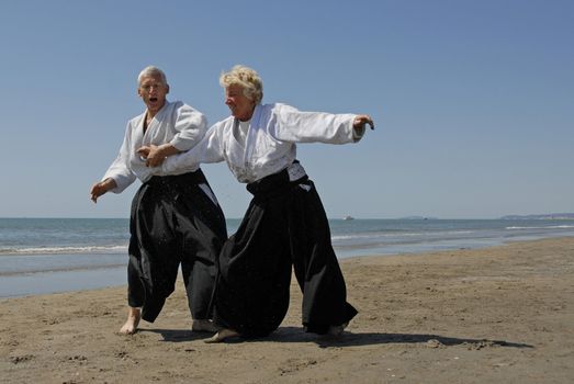 Two adults seniors are training in Aikido on the beach