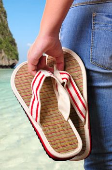 Girl holding sandals on the first day of vacations at the beach.
