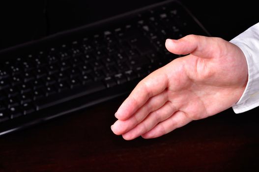 Hand ready for an handshake next do a computer keyboard on a dark table
