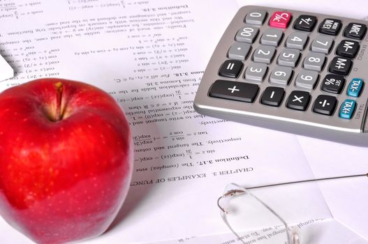 Maths exercices with a calculator, glasses and a red apple nearby.