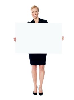 Female business promoter holding white blank banner ad with both hands and smiling at camera