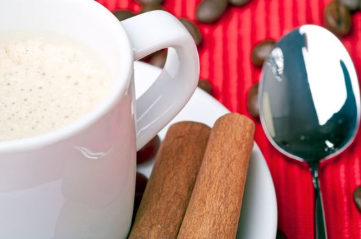 Coffee cup with cinnamon, coffee grains and a spoon by the side.