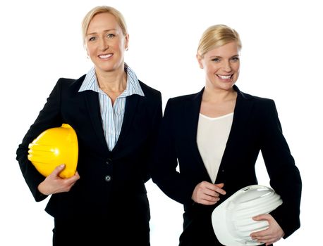 Young female architects holding hard-hats and posing against white background