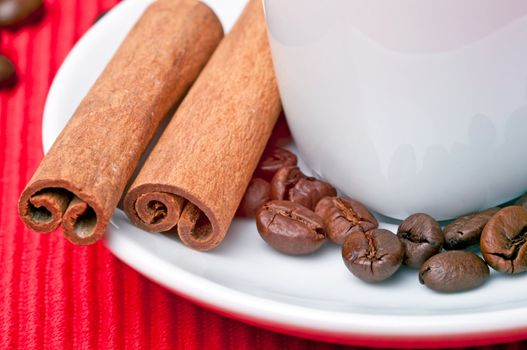 Coffee cup with cinnamon, coffee grains and a spoon by the side.