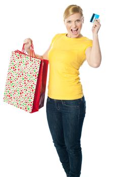 Happy shopaholic girl showing credit card, carrying paper bag