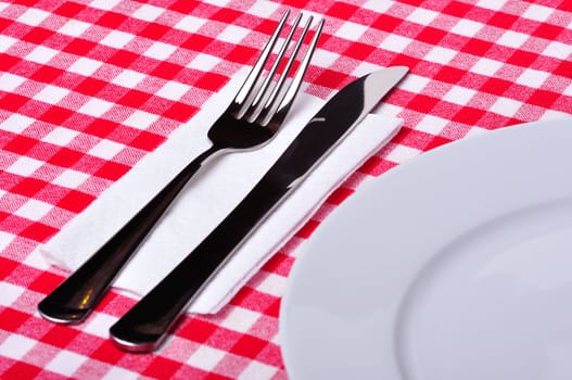 Fork, knife and plate on a table with a red and white tablecloth.