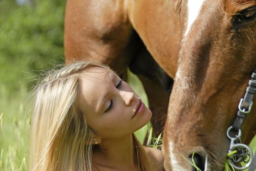 young blond teenager and her brown stallion in a field