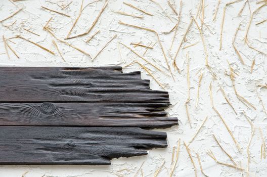 A background of a wall with black planks, white plaster and straw