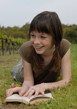 young girl reading a book laid down in a field