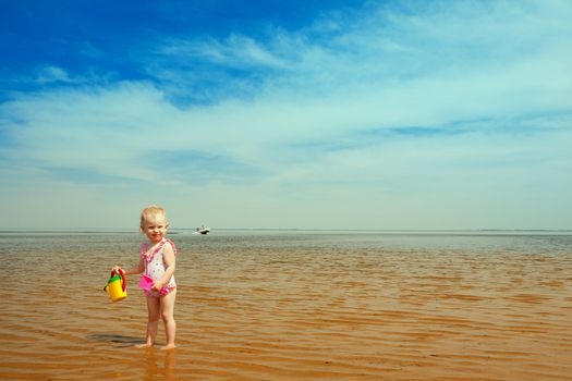 toned image - small girl with watering-pot on the seashore