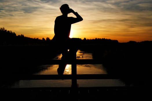 A person sitting on a brigde and making a call