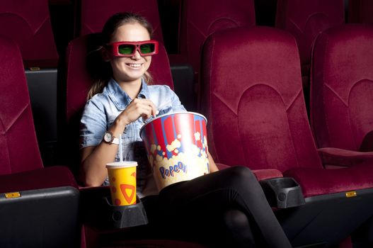 beautiful woman in a movie theater, watching a movie and drink a drink