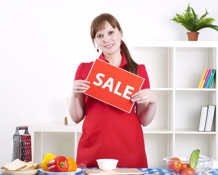 Young woman cooking fresh meal at home and holding sale sign