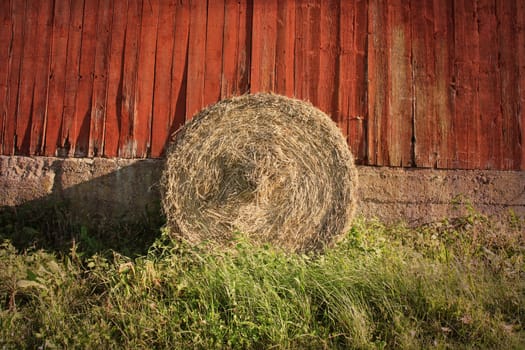 A single bale of hay against a wall of a red weathered barn. In vintage style.