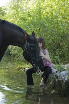 young teenager are kissing her black horse in a river