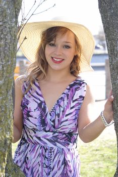 A young woman stands in the sunshine next to a tree.