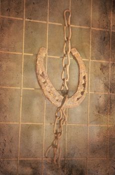 Grungy lucky horse shoe hanging in a chain on a rebar. Rusty and vintage look.
