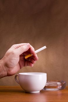 Hand holding a cigarette and a cup ashtray.