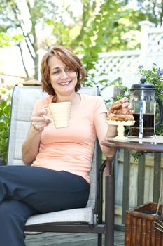 Happy woman relaxing with coffee and cookies on deck chair in backyard at home