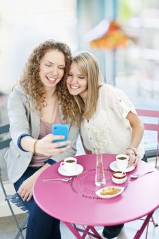 Two smiling women looking at smart phone in cafe