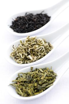 Black, white and green dry tea leaves in spoons