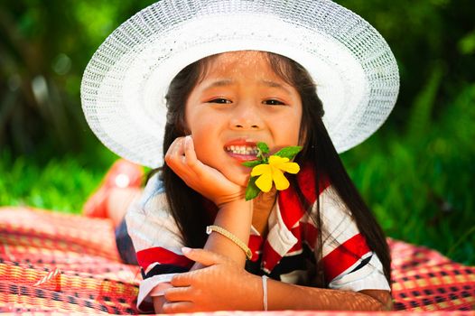 Young girl lying on a meadow with a hat on her head and a flower in the mouth