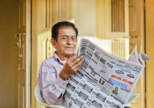 Senior Indian gentleman portrait outside his hinterland village home reading the local language morning newspaper on his front patio, editorial, Gujarat, India - February 27, 2012