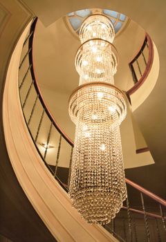 Vertical of long chandelier lighting spiral staircase with hardwood hand rial