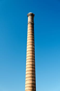 Iindustrial brick chimney against bright blue sky.