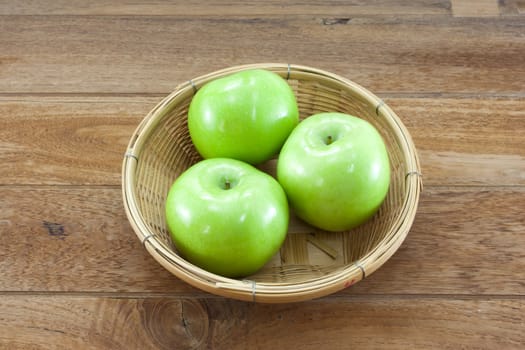 3 green apples on basket with teak wood background.