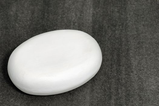 Spa or other hygiene concept: detailed macro shot of a white bar of soap contrasted on dark stone tiles as copy space.