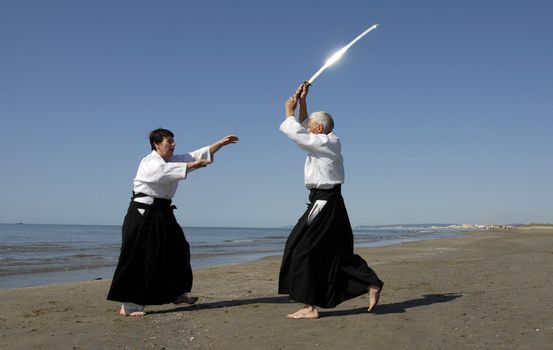 Two adults are training in Aikido on the beach