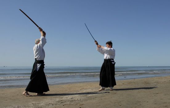 Two adults are training in Aikido on the beach